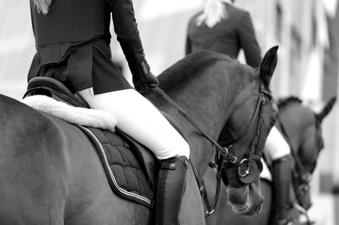 Black and white close-up of a rider in the saddle, boots and reins