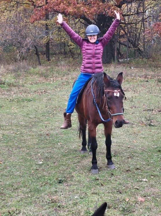 Rider in the saddle with both arms up, reins dropped, autumn woods